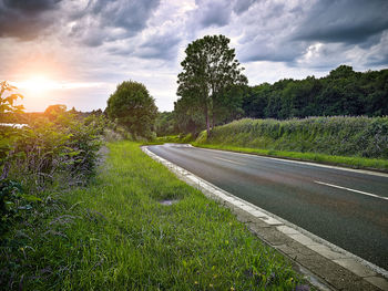 Road passing through field against cloudy sky