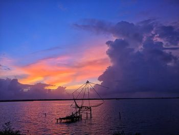 Chinese fishing nets in sea against sky during sunset