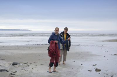 Rear view of friends standing on beach against sky