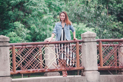 Portrait of woman standing by railing against trees