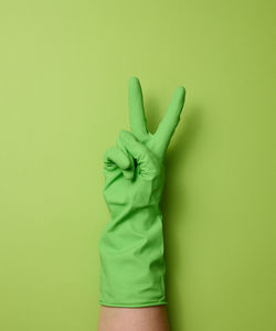 Hand in a rubber green glove for cleaning on a green background, part of the body is raised up