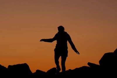 Silhouette woman standing on rock against orange sky