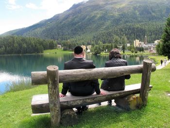 Rear view of men sitting by lake against mountain