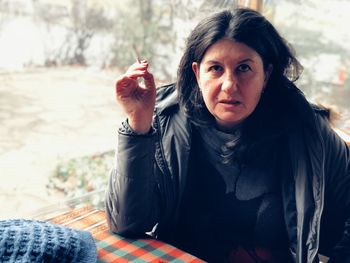 Mature woman looking away while holding cigarette at table