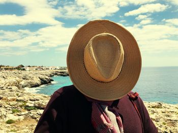 Rear view of man wearing hat at beach against sky