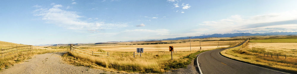 Road passing through agricultural field against sky