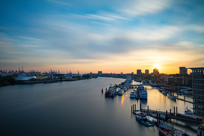 Boats moored in harbor at sunset