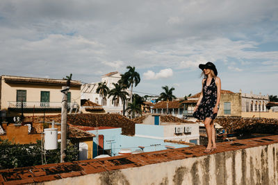 Smiling young woman standing on wall against cloudy sky