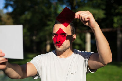 Man holding paper and red glass while standing in park on sunny day