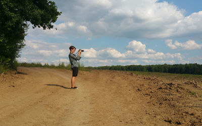 Side view of woman photographing while standing on land against sky