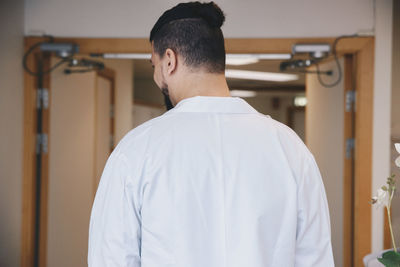 Rear view of young male doctor standing in hospital corridor