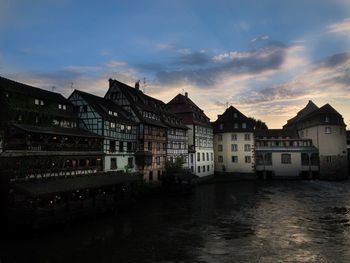 Buildings at waterfront against cloudy sky