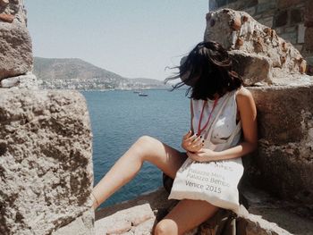 Woman sitting on rock by sea against sky