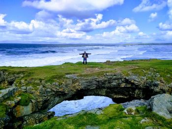 Man standing on rock by sea against sky