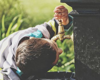 Close-up of boy drinking water over faucet