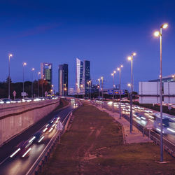 Illuminated street amidst buildings against sky at night