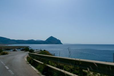 Scenic view of road by sea against clear sky