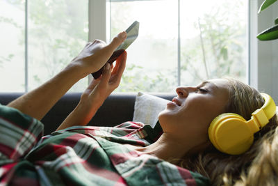 Woman using smart phone listening to music through headphones at home