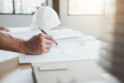 Cropped hand of engineer drawing blueprint at desk in office