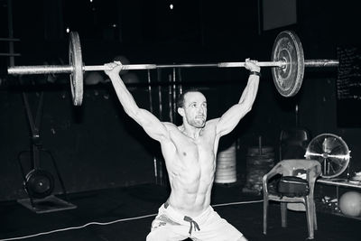 Shirtless fit young man working out with horizontal bar at indoors gym