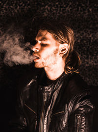 Close-up of young man smoking cigarette while standing outdoors at night