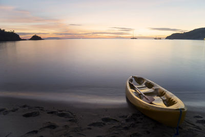 Boat moored on beach against sky during sunset