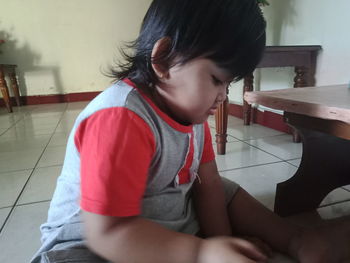 Cute girl looking away while sitting on tiled floor at home