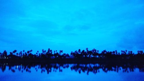 Reflection of silhouette trees in lake against sky at night