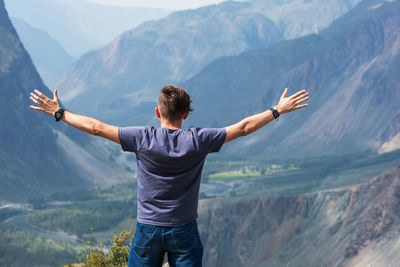 Rear view of man with arms raised standing on mountains