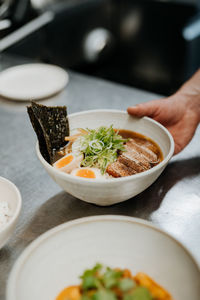 Hand of unrecognizable waiter serving asian noodle soup, ramen in white bowl