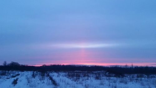 Snow covered landscape against sky during sunset