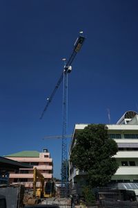 Low angle view of crane by building against blue sky