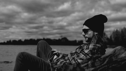 Side view of man reclining against cloudy sky