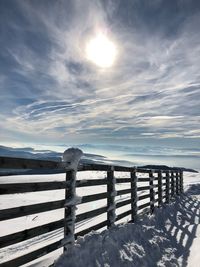 Wooden post on snow covered land against sky