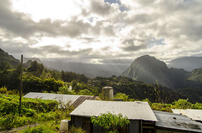 Houses by mountains against cloudy sky