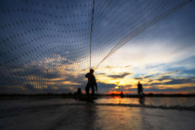 Silhouette men on beach against sky during sunset