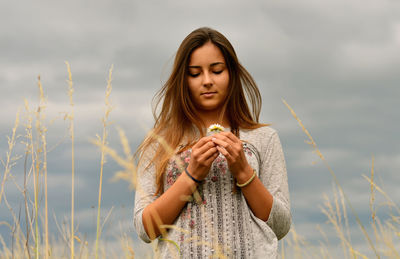 Beautiful young woman holding camera on field against sky