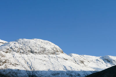 Low angle view of snowcapped mountains against clear blue sky