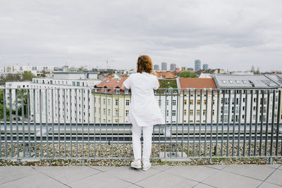 Full length rear view of senior female doctor leaning on railing looking at city