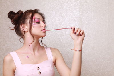 Young woman with pink make-up chewing gum against wall