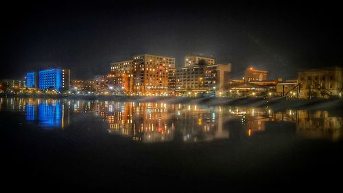 Illuminated buildings by sea against sky at night