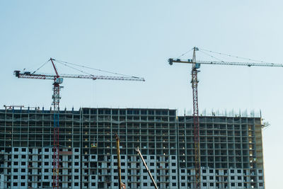 Low angle view of crane by building against clear sky