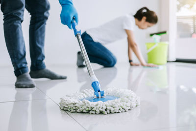 Low section of couple cleaning tiled floor at home