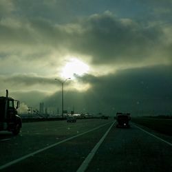 Cars on road against cloudy sky