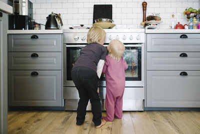 Rear view of siblings looking at oven in kitchen