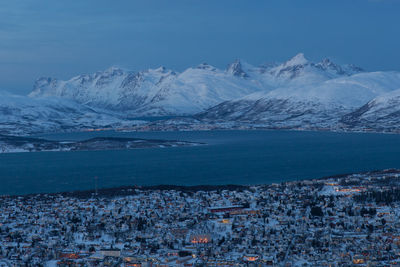 Town by fjord with snowcapped mountains against sky