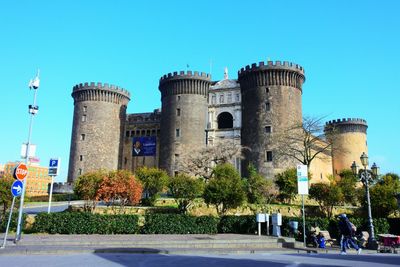 People by historic building against clear blue sky