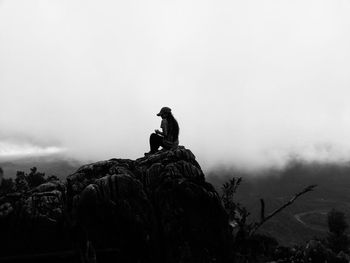 Woman sitting on rock against sky