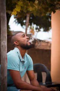 Young man looking away while sitting on tree