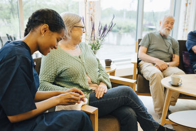 Young female caretaker filing senior woman's nail while sitting at nursing home